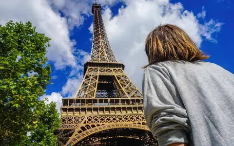 Persona admira la imponente Torre Eiffel bajo un cielo azul con nubes.