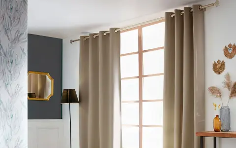 Eine schicke Gardinenstange anbringen, um die beige Vorhänge über dem Fenster zu befestigen. Dekorative Elemente wie Spiegel und Pflanzen ergänzen den Raum.