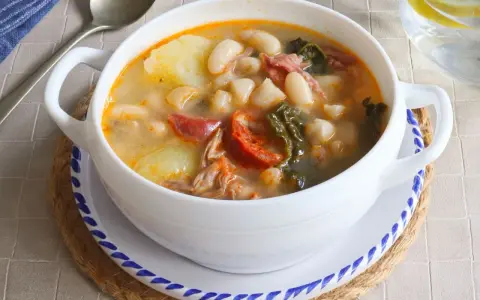 Un tazón blanco de caldo gallego con patatas, alubias, chorizo y grelos.