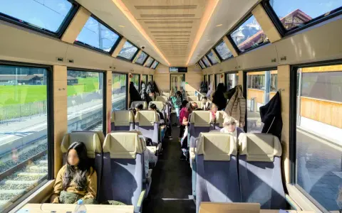 Passengers enjoy the scenic views from the panoramic windows of a train on the Golden Pass Line, with mountains visible outside.