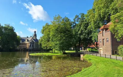 Ein idyllischer vechte radweg führt vorbei an einem Teich, grünen Bäumen und einem historischen Wasserschloss.