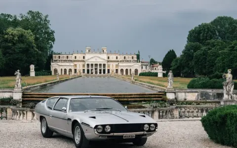 Srebrny Lamborghini Espada z lat 70. przed okazałą willą z basenem i rzeźbami.