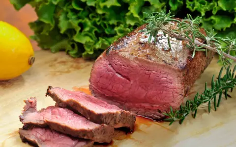 Saftiges Roastbeef mit perfekter kerntemperatur medium, garniert mit Rosmarin. Daneben ein Zitronen- und Salatblatt.