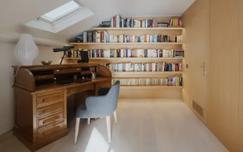 Scrivania in legno massiccio e libreria moderna illuminata, un perfetto esempio di come abbinare e mischiare arredamento classico e moderno in uno studio mansardato.