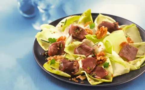 Salade de gésiers savoureuse avec endives croquantes, noix et persil frais, assaisonnée d'une vinaigrette aux graines.