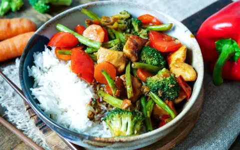 Schüssel mit Reis und einem bunten Chop Suey aus Hühnchen, Brokkoli, Karotten, Paprika und grünen Bohnen.