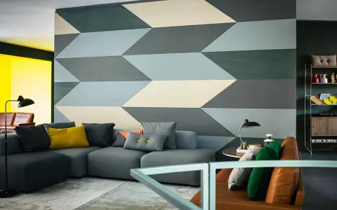 Un salon moderne avec un canapé gris et un mur orné d'un motif géométrique audacieux. Une idée motif peinture murale qui crée une illusion de profondeur.