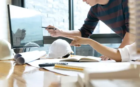 Deux architectes discutent d'un plan sur un écran, utilisant un système de gestion de contenu d'entreprise pour organiser leurs documents.