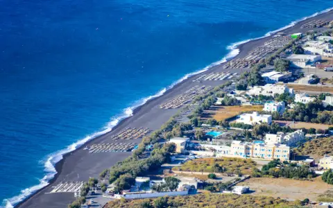 Santorini plaże z czarnym piaskiem, rzędy leżaków i białe budynki hotelowe nad turkusowym morzem.