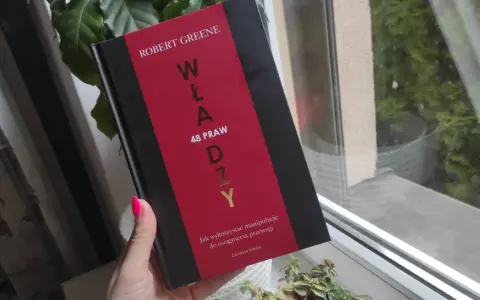 Dłoń z neonowym różowym lakierem trzyma książkę "48 praw władzy" Roberta Greene'a.