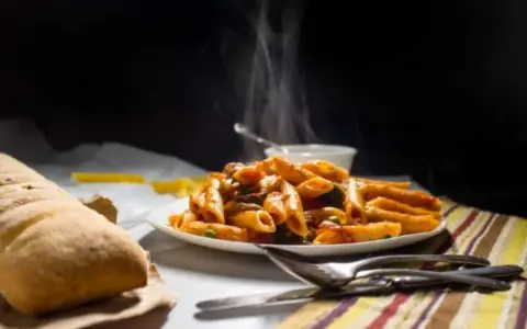 Piatto fumante di penne alla vodka, con pane croccante e posate. Un classico confortante.