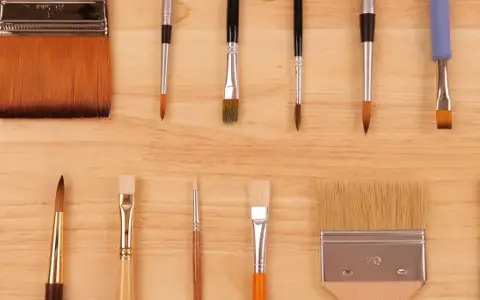 Collection de différents types de pinceaux peinture, ronds et plats, aux poils variés, disposés sur un fond en bois.