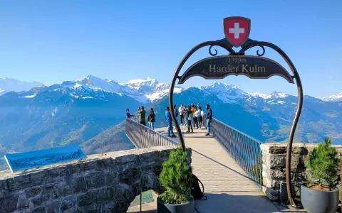 Tourists enjoy the breathtaking panorama from the Harder Kulm viewpoint, with snow-capped mountains under a clear blue sky.