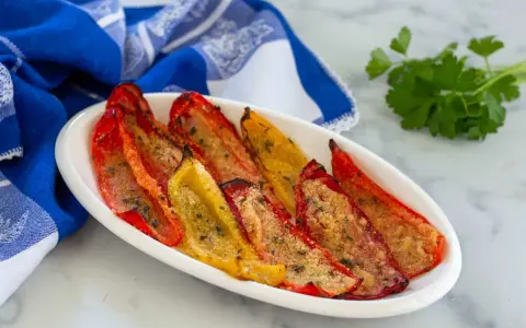 Peperoni gratinati al forno, rossi e gialli, cotti alla perfezione con pangrattato e erbe aromatiche, serviti su un piatto bianco con un tovagliolo blu.
