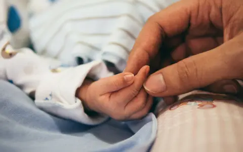 Dłoń rodzica obejmuje maleńką dłoń dziecka. To symbol miłości i troski, a także przygotowań do złożenia wniosku o urlop macierzyński.