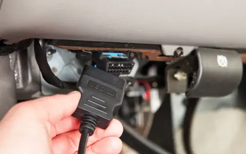 Ręka podłącza kabel OBD II do złącza diagnostycznego pojazdu, aby sprawdzić błędy DTC.