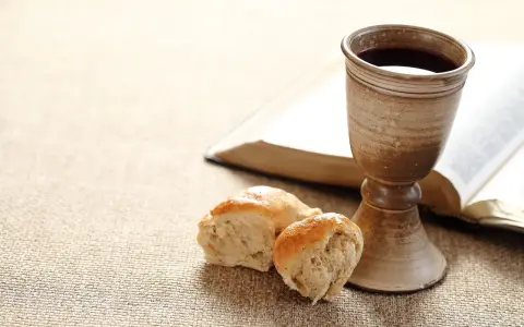 Kelch mit Rotwein, Brot und aufgeschlagenes Buch. Symbol für das christliche Abendmahl und dessen Bedeutung im Glauben.