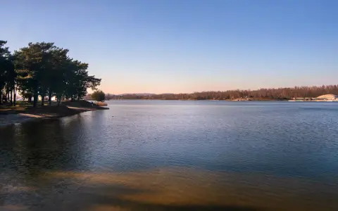 Spokojne jeziora w Małopolsce o zachodzie słońca. Drzewa na brzegu rzucają długie cienie na piaszczystą plażę.