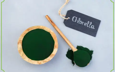Chlorella tabletki na co pomaga? Zielony proszek w miseczce i na łyżce, obok tabliczka z napisem "Chlorella".