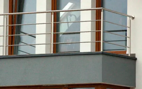 Nowoczesne mocowanie balustrady od czoła balkonu, wykonane ze stali nierdzewnej, z widocznymi czterema poziomymi prętami.