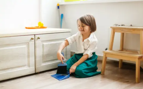 Niña practicando vida práctica Montessori, barriendo el suelo con escoba y recogedor.