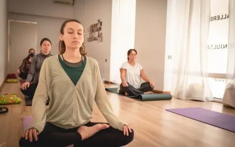 Mujeres meditando en clase de yoga. Una de ellas, en primer plano, parece estar en el **primer trimestre de embarazo**, buscando calma y conexión.