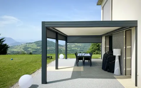 Pergola bioclimatique moderne face à un paysage vallonné. Le vent fort fait onduler les lames du toit, créant des jeux d'ombre et de lumière.