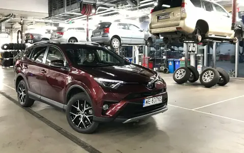Czerwona Toyota RAV4 w serwisie. W tle inne auta na podnośnikach. Zastanawiasz się nad toyota trzeci przegląd gwarancyjny cena?