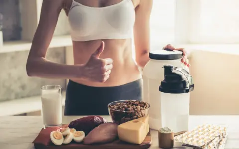 Kobieta z kciukiem w górę prezentuje produkty wspierające dietę wysokobiałkową: mięso, rybę, jajka, ser, orzechy, mleko i suplementy.