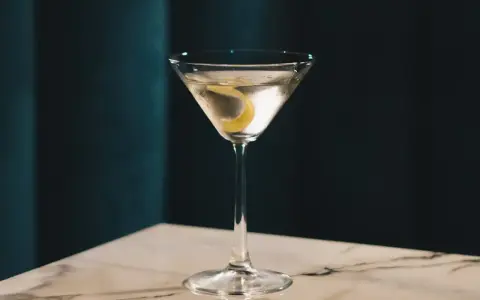Elegancki gin z wermutem, ozdobiony skórką cytryny, czeka na stole z marmurowym blatem.