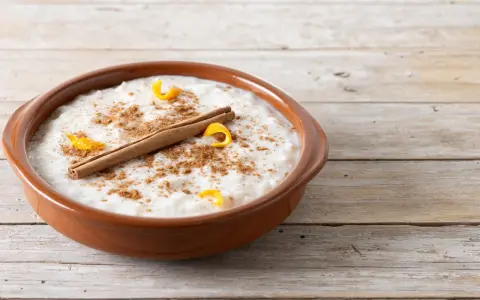 Un tazón de arroz con leche cremoso, espolvoreado con canela y adornado con cáscara de naranja y una rama de canela.