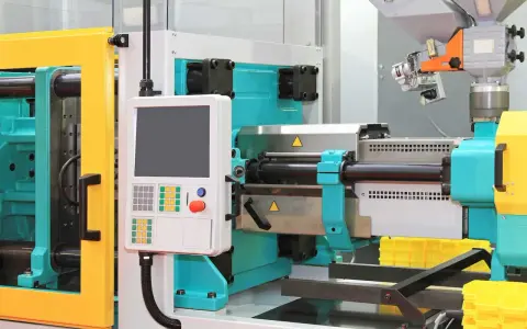 A modern low volume plastic injection molding machine with a control panel and yellow safety guards.