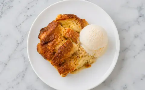 Un délicieux pain perdu au four, doré et moelleux, servi avec une boule de glace à la vanille sur une assiette blanche.