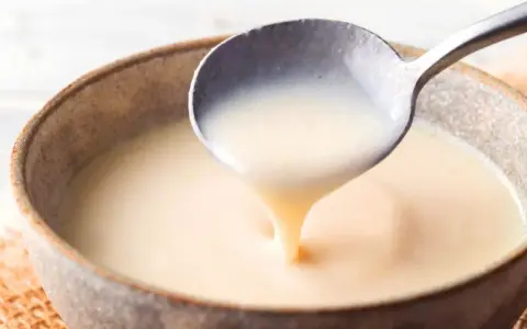 Cuchara sirviendo crema inglesa espesa y suave en un cuenco rústico.