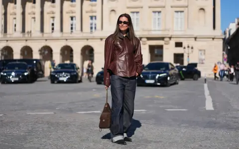 Elegancka kobieta w skórzanej kurtce i jeansach, z brązową torebką na ramieniu. Jej filigranowa figura podkreślona jest przez luźne spodnie i dopasowaną górę.