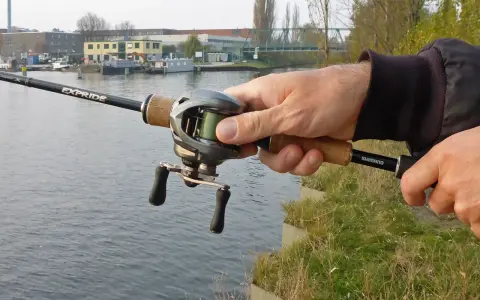 Hand hält Angelrute mit Baitcast-Rolle, die grüne baitcast schnur ist gut sichtbar.