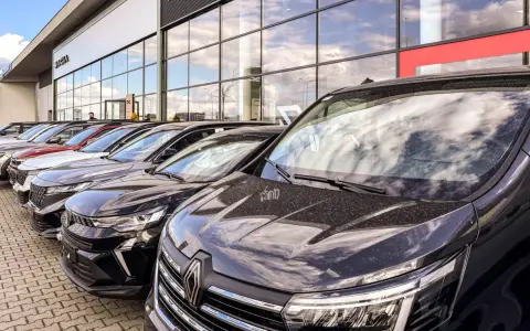 Rząd nowych samochodów na placu. W tle budynek salonu Dacia. Sprawdź autoplac opinie przed zakupem.