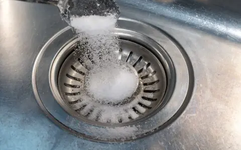 Salt hälls ner i diskhoavloppet. En skopa med salt sprids över silen.
