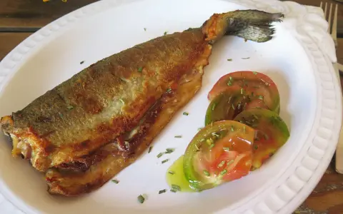 Trucha a la navarra dorada y crujiente, servida con rodajas de tomate fresco y hierbas aromáticas.