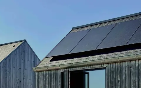 Mörka träfasader möter tak med solpaneler. En modern, hållbar design som fångar solens energi, nästan som en denim solar-dröm.