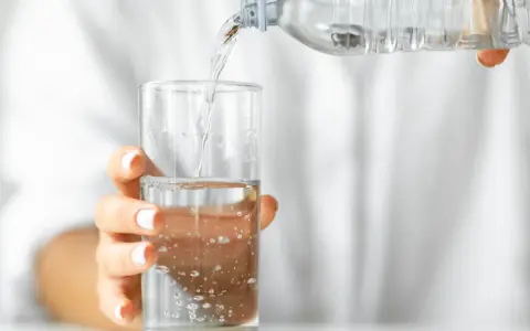 Eine Hand hält ein Glas, in das kohlensäurehaltiges Mineralwasser gegossen wird.