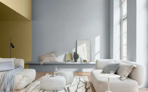 Sala de estar con paredes en tonos grises y mostaza, muebles claros y alfombra con diseño orgánico. Ideales colores suaves para pintar una casa.