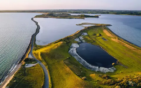 Grönskande landskap med en slingrande väg längs kusten i Danmark. En vy som från ett utkikstorn Danmark, med vatten och fält.