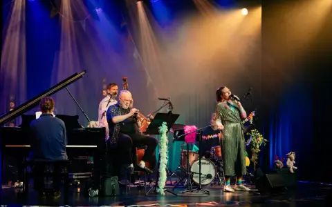 En jazzgrupp uppträder på scenen under Stockholm Jazz Festival. En sångerska i glittrig klänning sjunger, en man spelar trumpet, en annan står vid basen och en person sitter vid pianot.