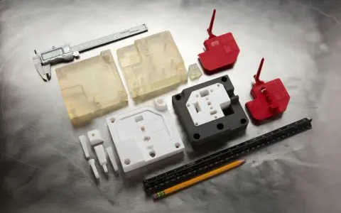 Various 3d printed molds, including clear, white, and red plastic components, are laid out with a caliper, ruler, and pencil on a metallic surface.