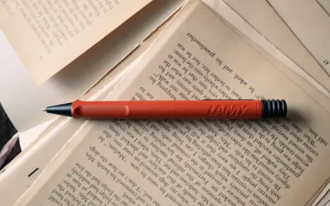 Un stylo rouge Lamy repose sur des pages jaunies. Force est de constater que la lecture et l'écriture font partie de notre histoire.