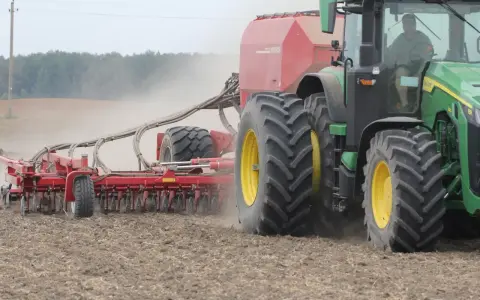 Zielony traktor z siewnikiem Horsch pracuje na polu. Trwa czas orki 1 ha, widać kurz unoszący się z ziemi.