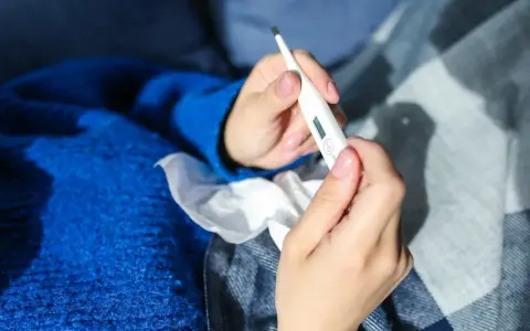 Dłonie trzymające termometr, chusteczki i niebieski sweter. Może to być objaw choroby, np. liszajec ICD-10.