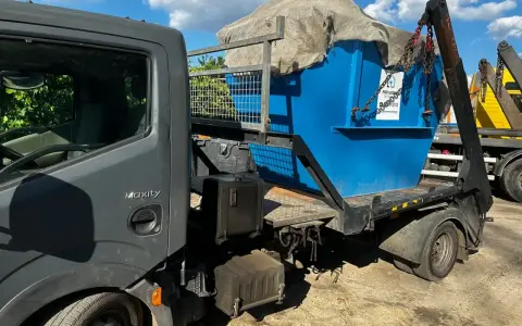Niebieski kontener na śmieci, przykryty płachtą, jest ładowany na ciężarówkę. Czy PCV to plastik? Tak, to rodzaj plastiku.