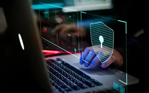 Mano sobre teclado de portátil, con un escudo digital de ceros y unos, simbolizando la seguridad informática.
